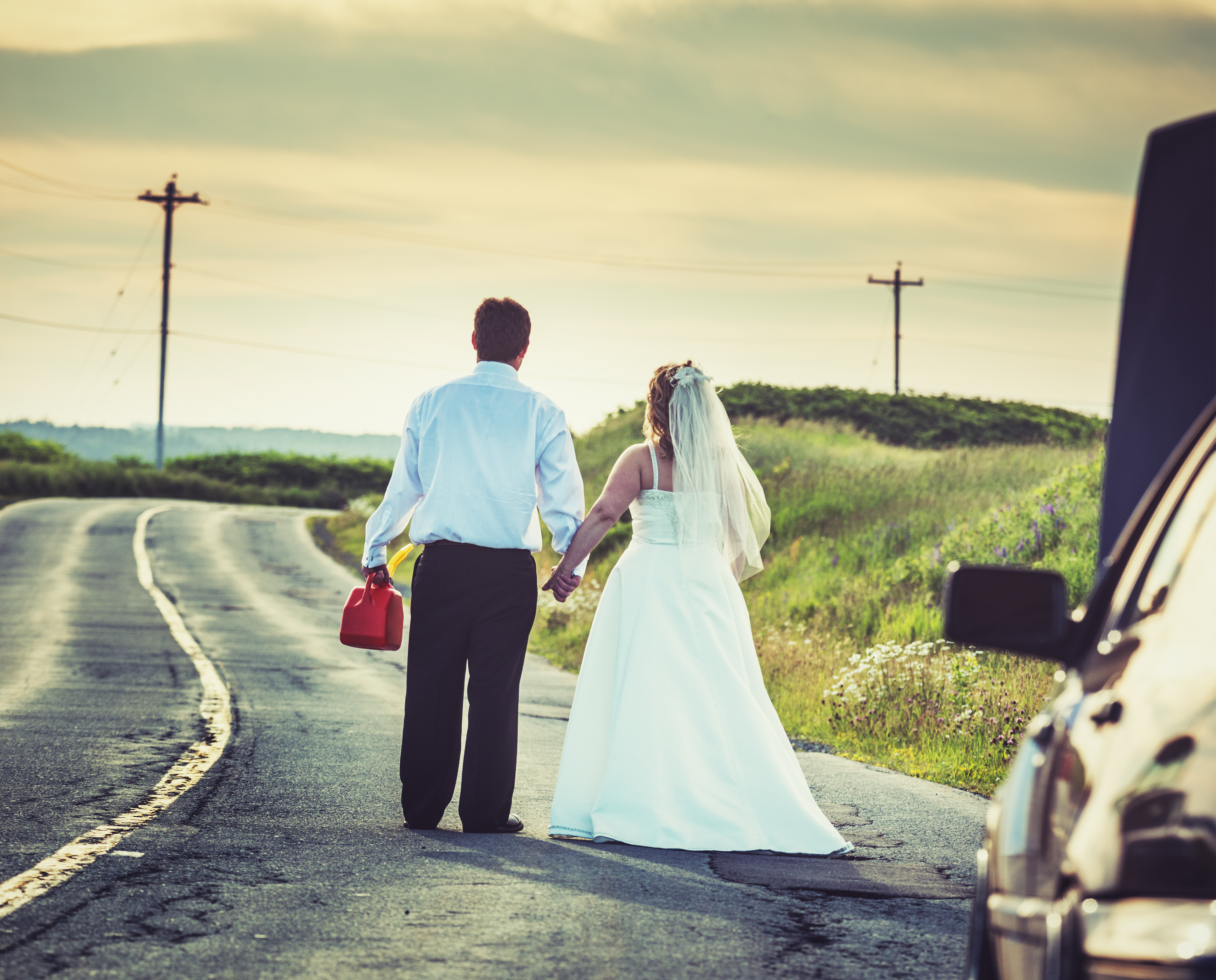 Newly wed couple stuck without petrol on the side of the road holding an empty petrol tank